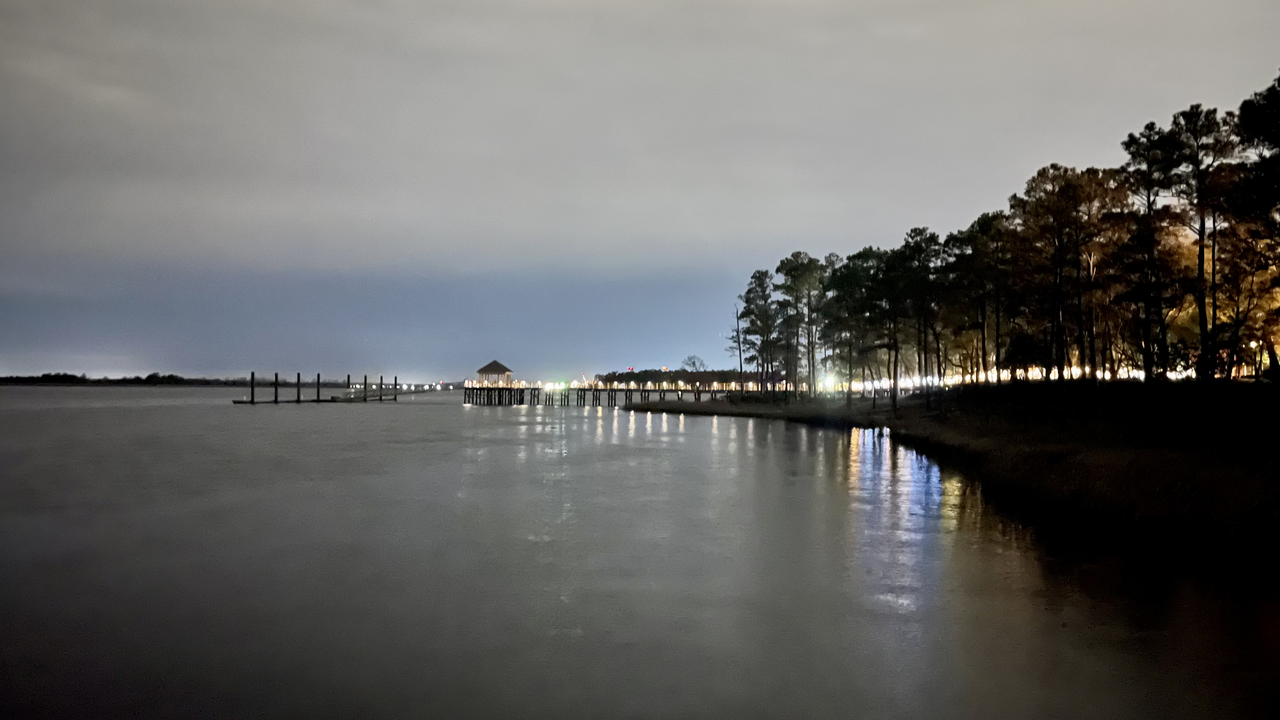 Atmospheric pier at night with city lights along the shoreline