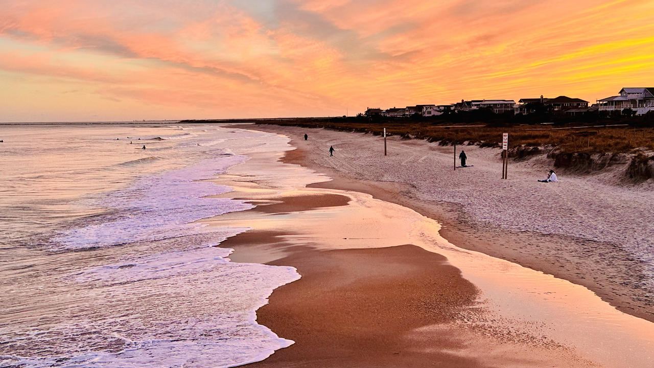 Wrightsville Beach sunset with dramatic peach and pink clouds, surfers in the surf